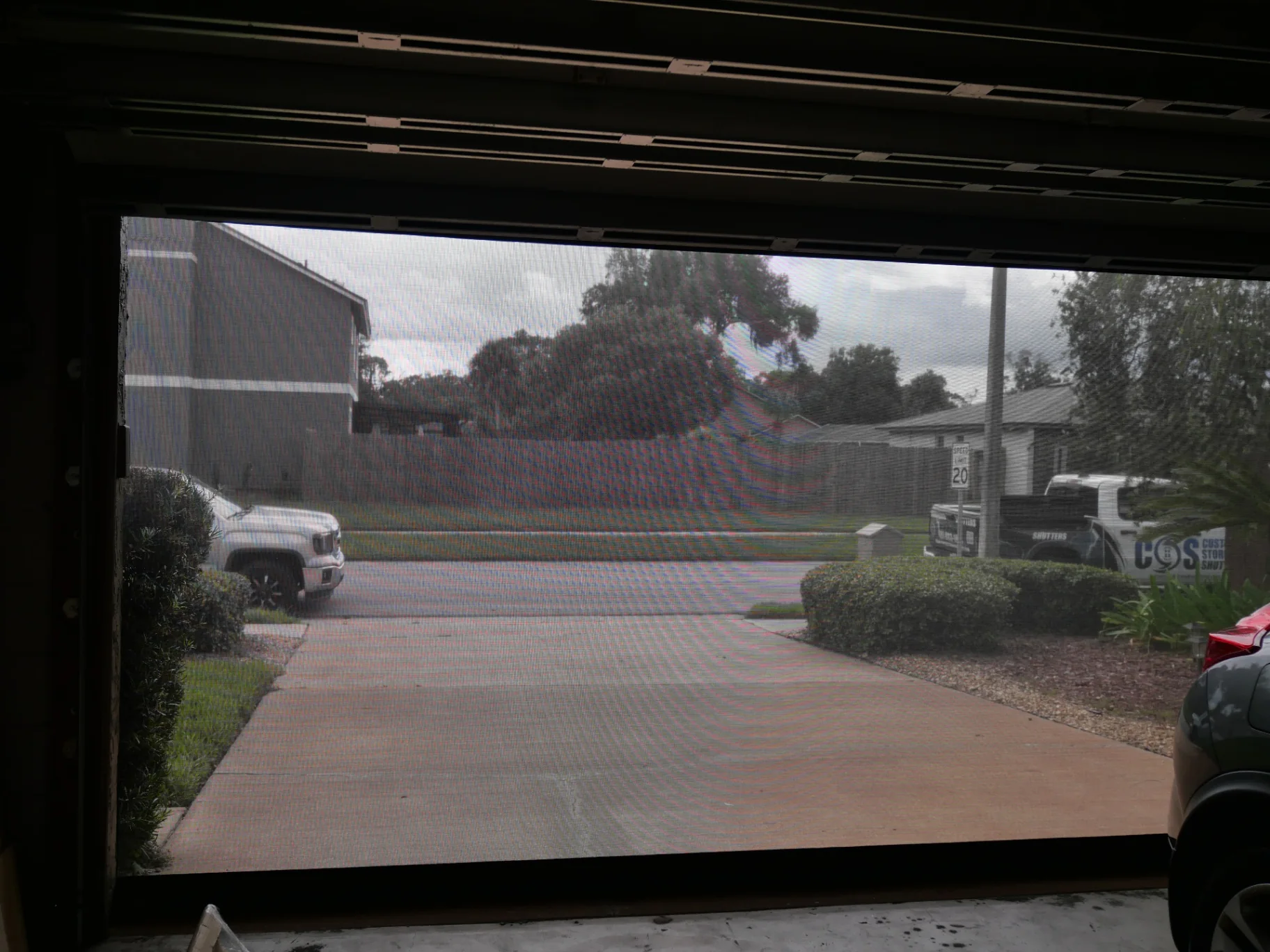 Black retractable hurricane screen lowered across a garage opening beneath a bronze housing, viewed from inside