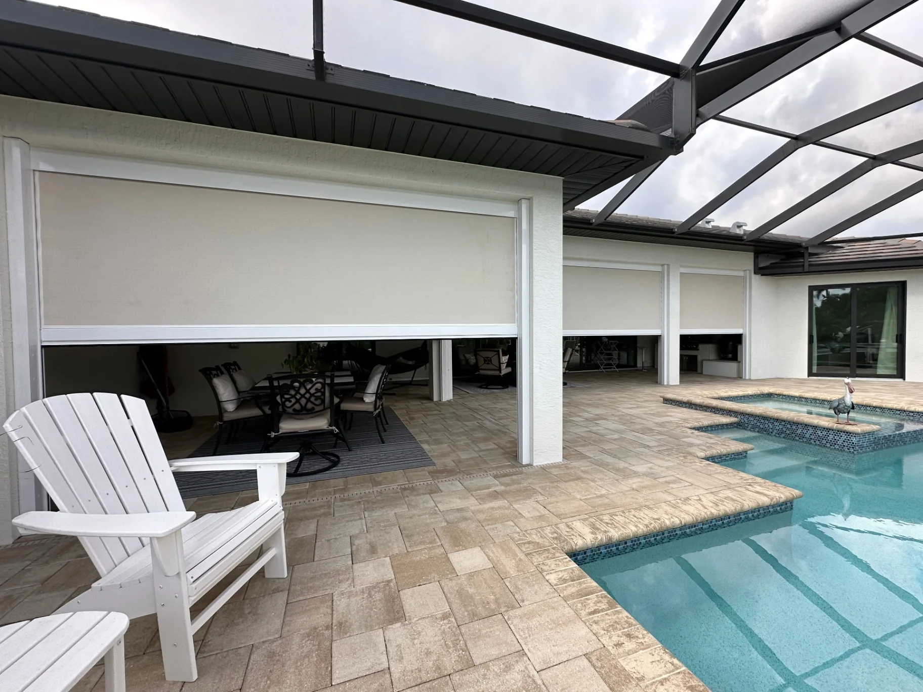White retractable hurricane screens partly lowered across several covered lanai openings beside a swimming pool