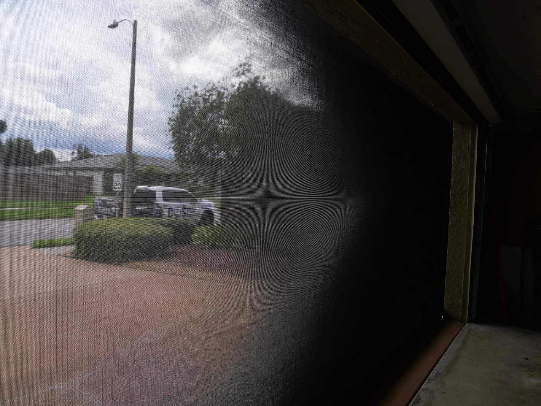 Black retractable hurricane screen lowered across a garage opening, viewed from inside at an angle