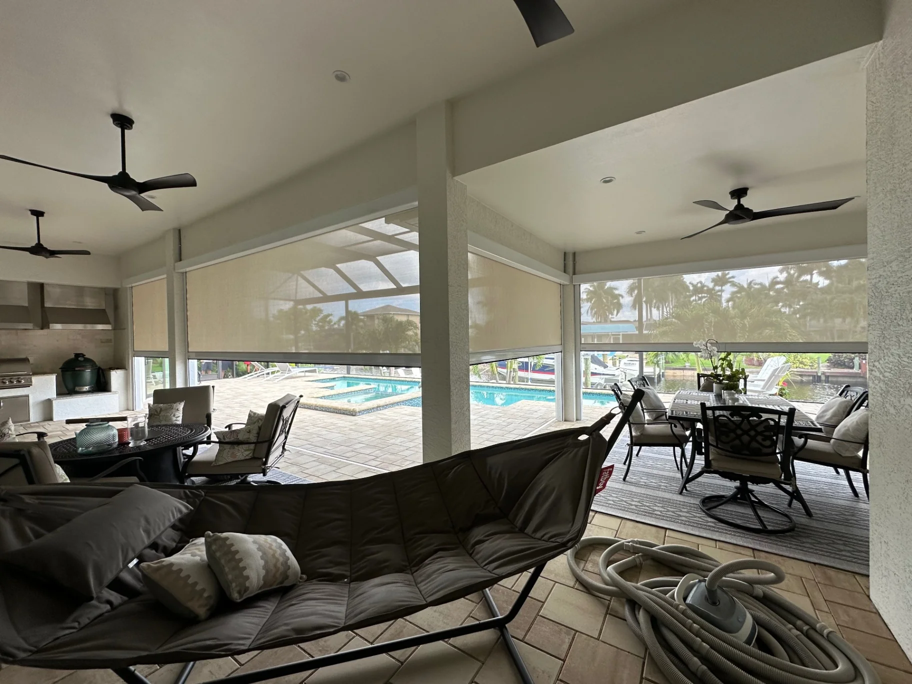 White retractable hurricane screens partly lowered around multiple openings of a covered pool lanai, viewed from inside