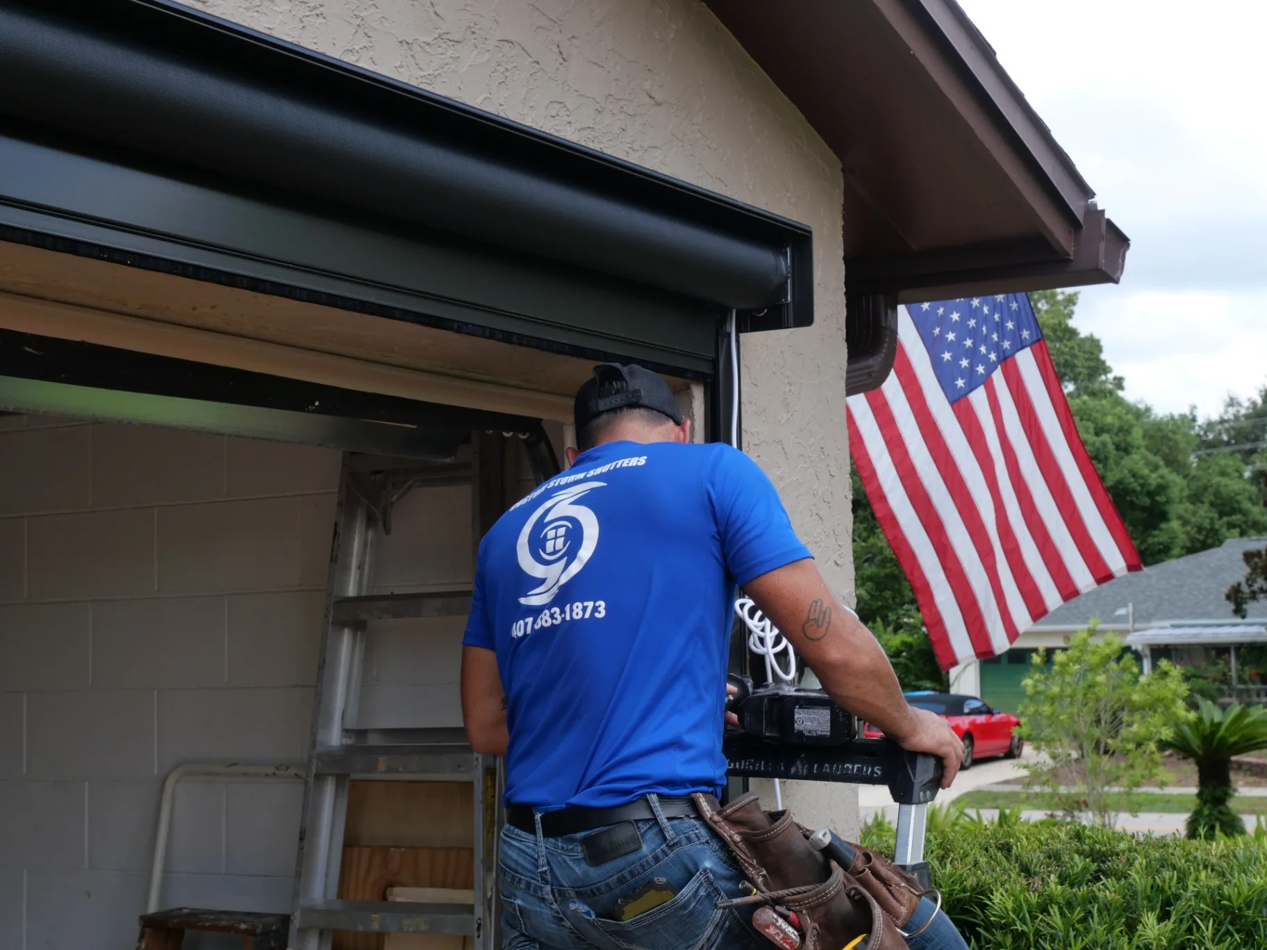 Installer working beneath a bronze retractable hurricane-screen housing above a garage opening
