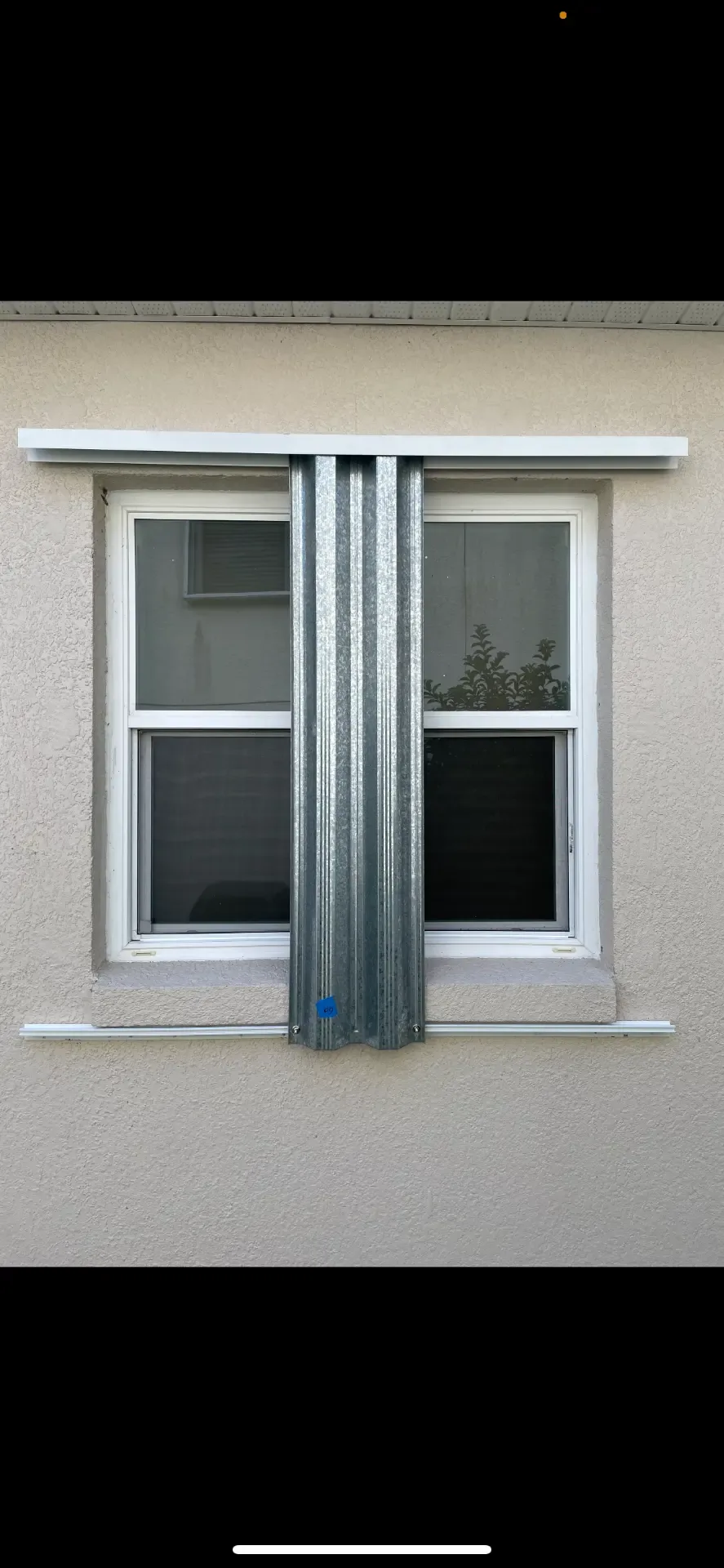 Galvanized steel storm panels partially stacked between two windows on a stucco home