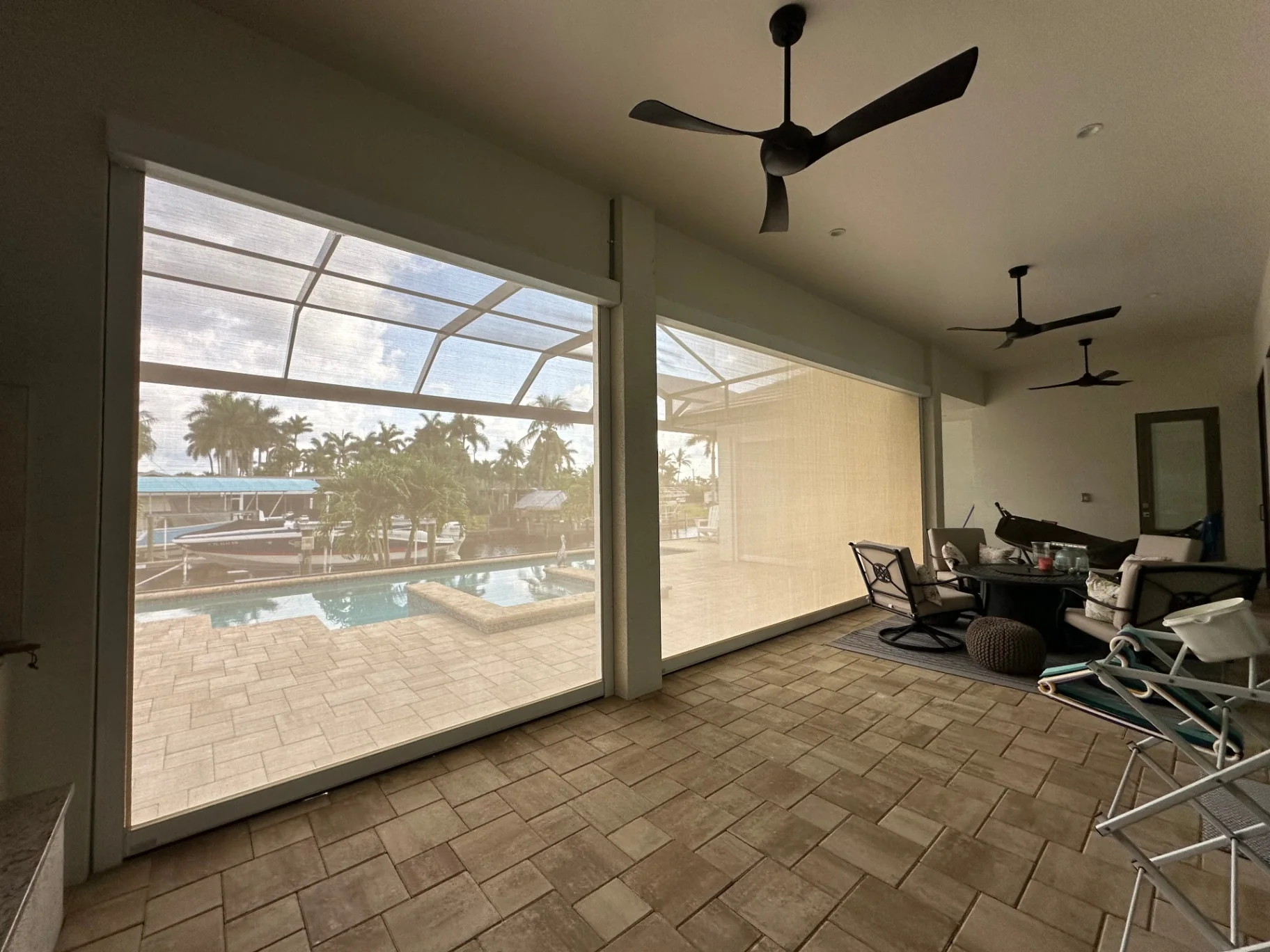 White retractable hurricane screens lowered across two covered lanai openings overlooking a pool and canal
