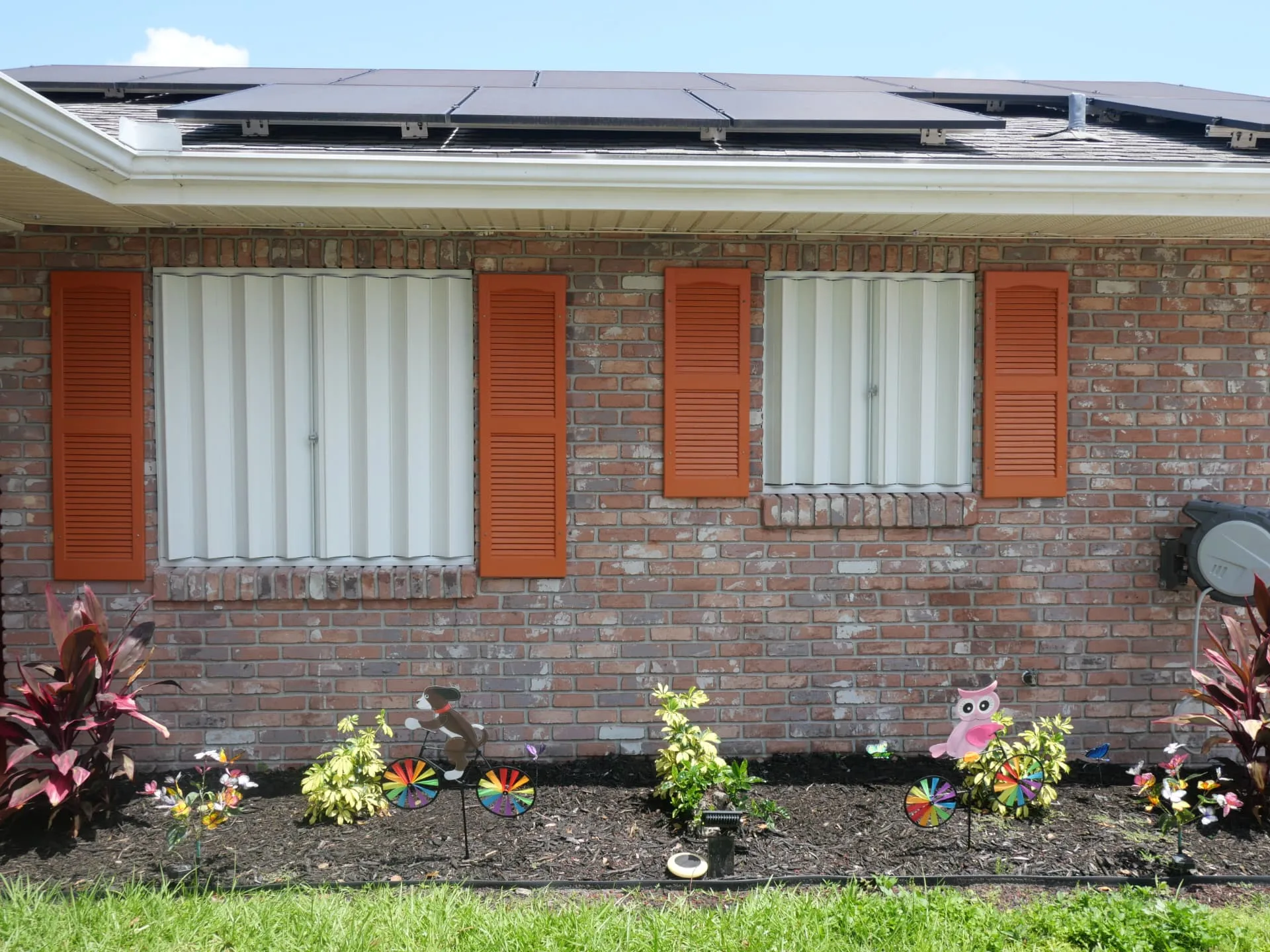 The same two front windows with the white accordion hurricane shutters closed across the openings
