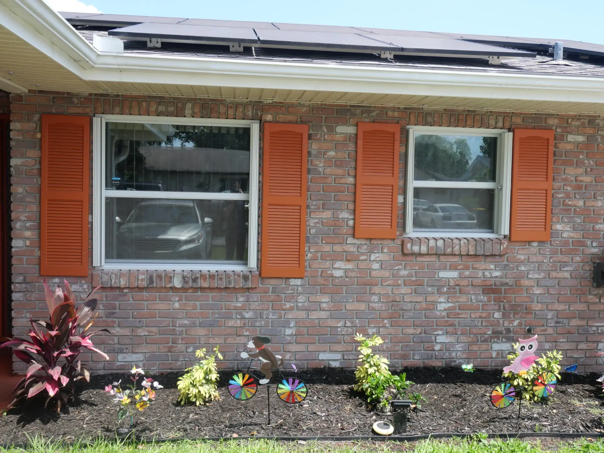 The same two front windows with the white accordion hurricane shutters fully open and stacked to the sides