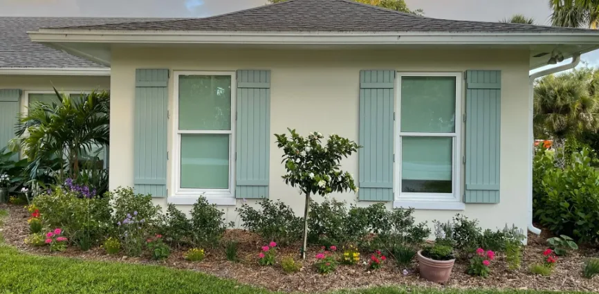 Product visualization of sage green Colonial shutters folded back on both sides of two windows on a cream Florida home